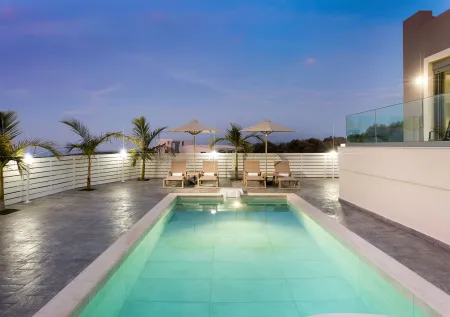 Fenced pool area with sunbeds and umbrellas during night time
